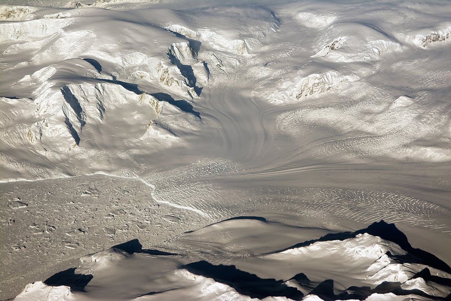Low sunlight illuminates glaciers and mountains in West Antarctica, casting long shadows over snow.